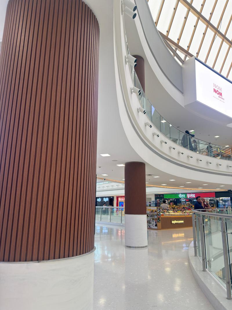 Wood-finish flexible louvers wrapping a round atrium column in a Navi Mumbai mall, supplied by Urbane Decor