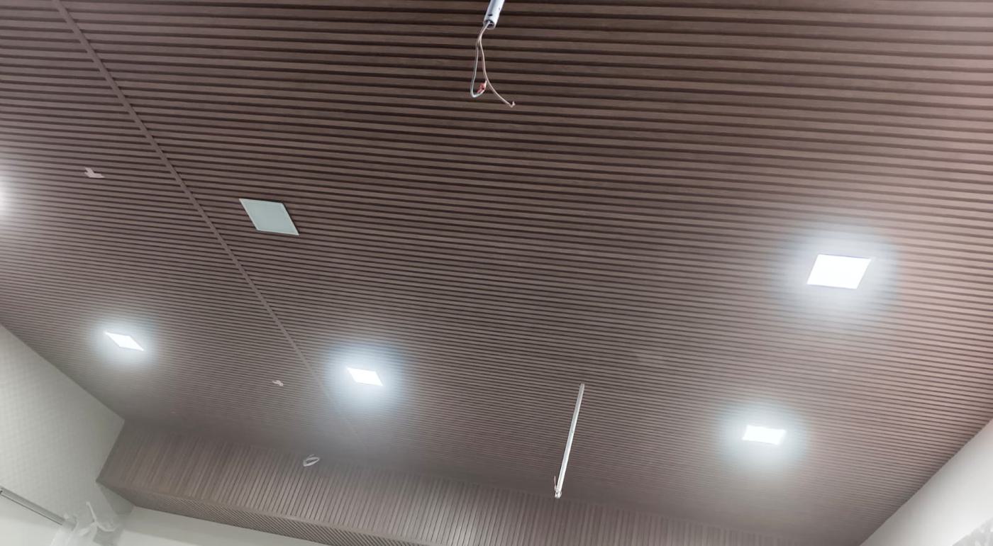 Wood-finish louvers installed across an office ceiling with recessed square lights