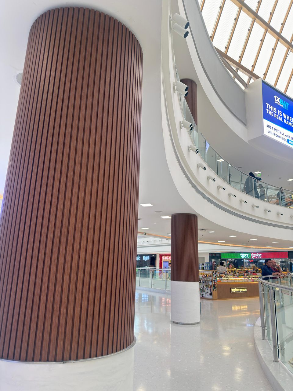 Wood-finish flexible louvers wrapping a tall round column in a Navi Mumbai mall atrium, supplied by Urbane Decor