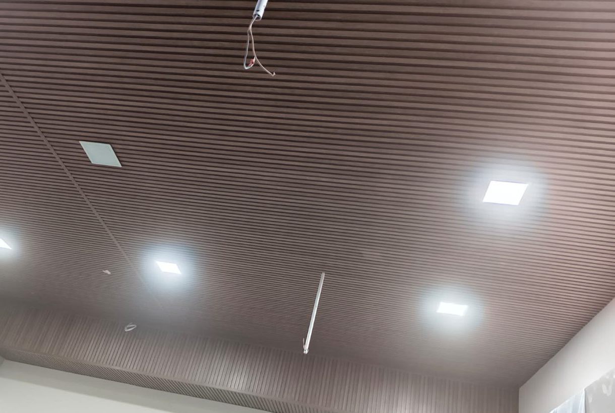 Dark wood-finish louvers fixed across a commercial ceiling with recessed square lights, a real Urbane Decor installation