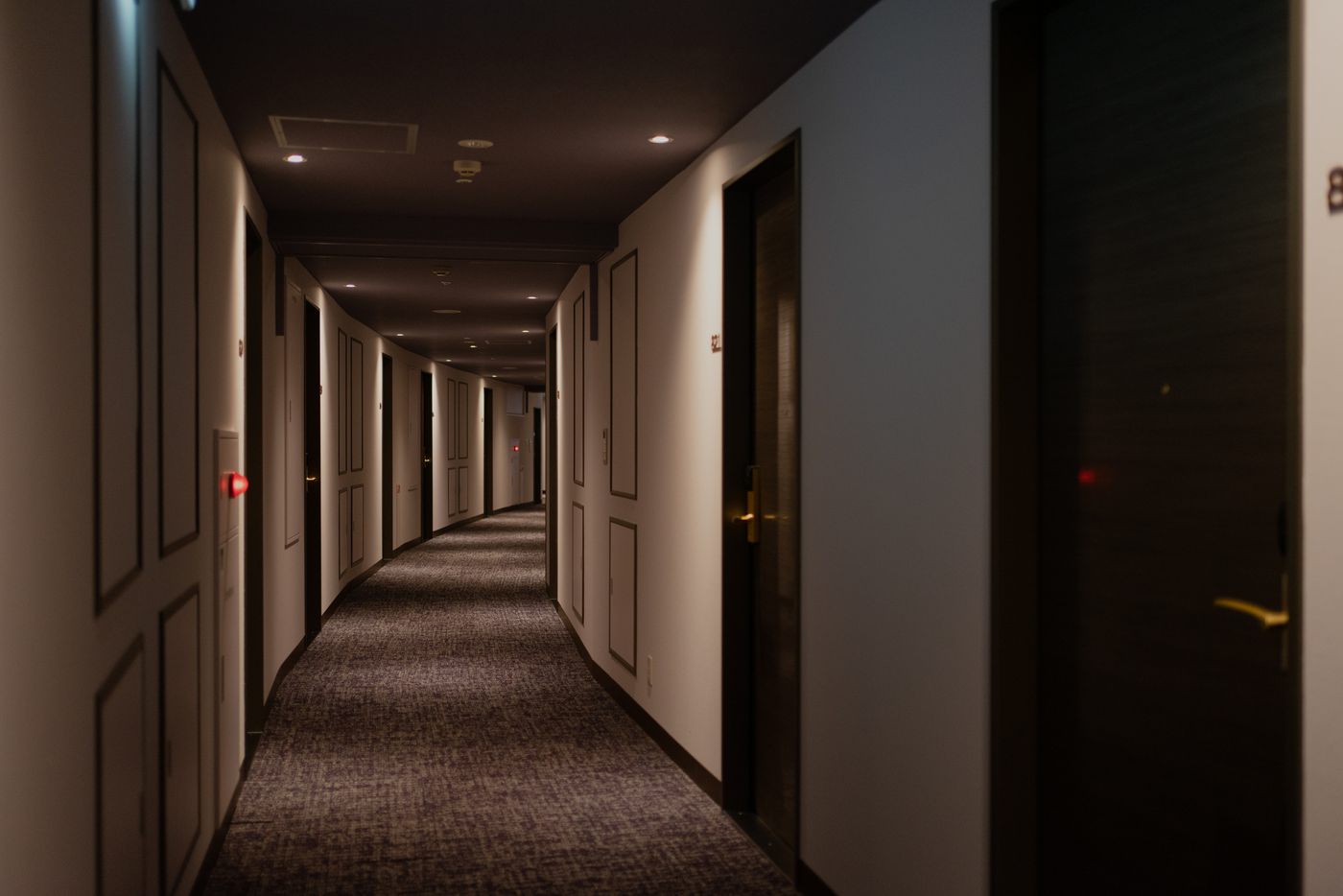 Long, dimly lit hotel corridor with dark panelled walls, patterned carpet and room doors on both sides