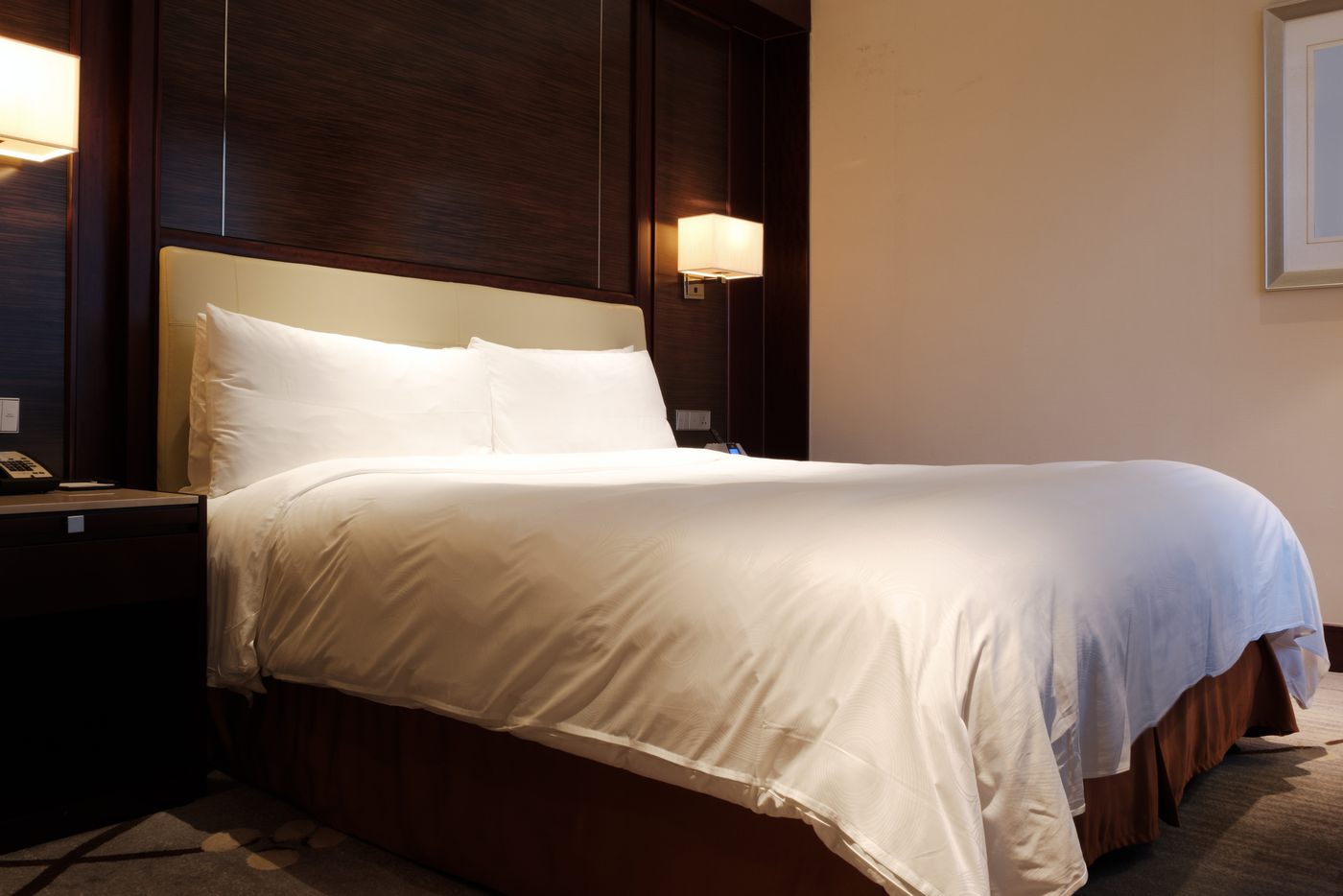 Hotel guest room with a dark wood-panelled wall behind the bed, white bedding and warm wall lights