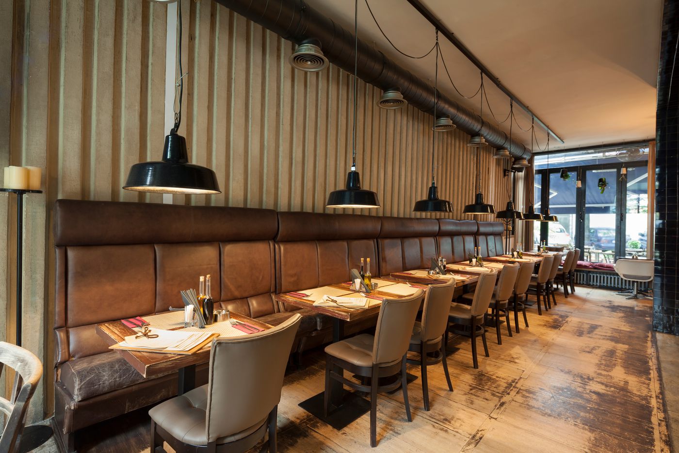 Restaurant with a long leather banquette against a tall vertical wood-slat wall under warm pendant lights