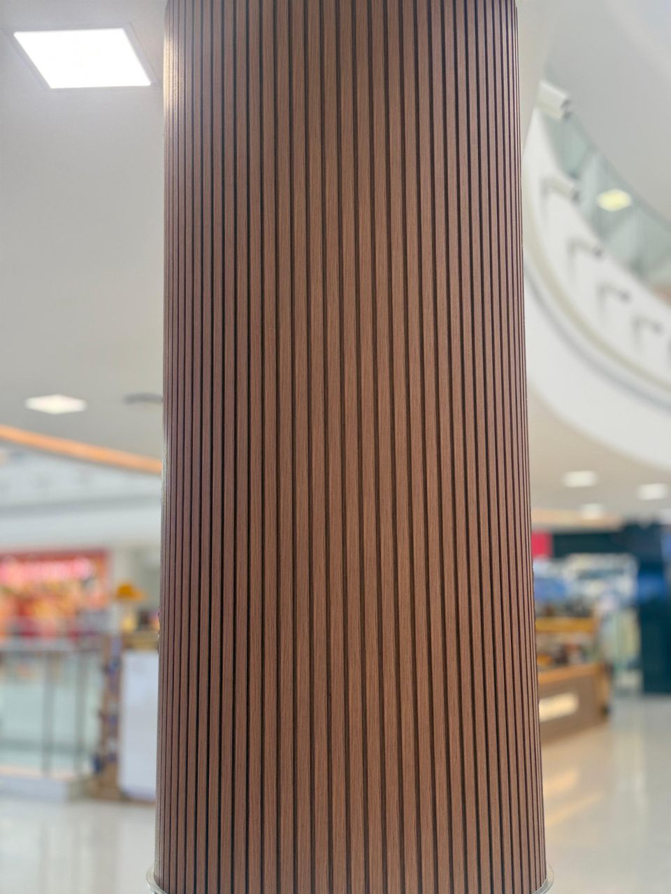 Wood-finish flexible louvers wrapped around a round mall column, a real Urbane Decor installation