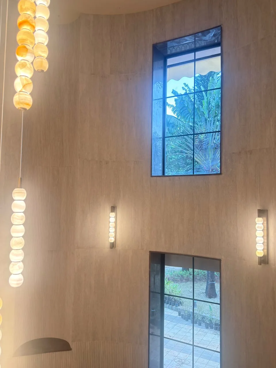 SoftIQ soft stone cladding a double-height hall with tall windows and glowing pendant lights in Lonavla, a real Urbane Decor installation